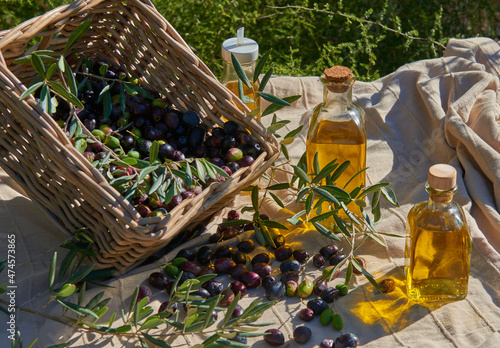 several bottles of oil next to a basket with ripe olives