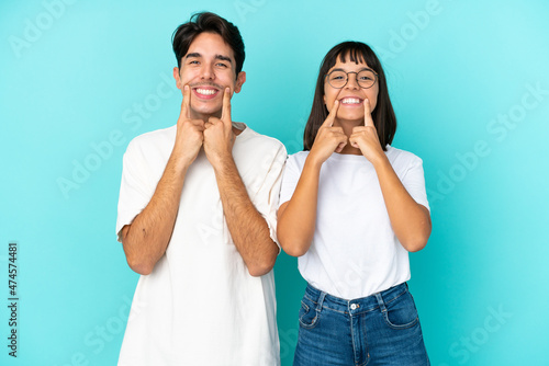 Young mixed race couple isolated on blue background smiling with a happy and pleasant expression
