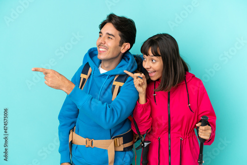 Young mountaineers couple isolated on blue background pointing to the side to present a product
