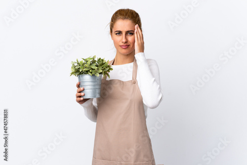 Young blonde gardener woman girl holding a plant over isolated white background unhappy and frustrated with something. Negative facial expression
