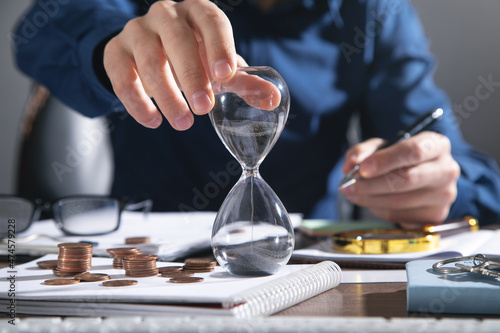 Businessman holding hourglass. Coins and business objects on the desk