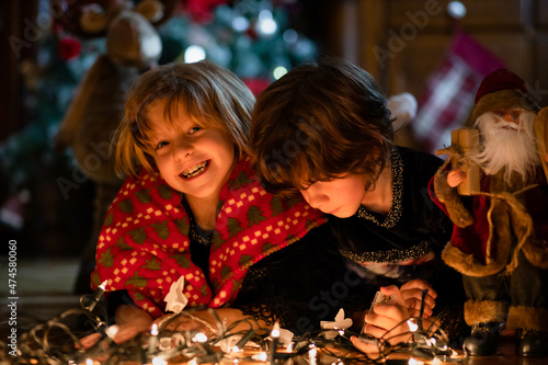 Little girls, sisters, lying on the floor with Christmas lights and Santa toy