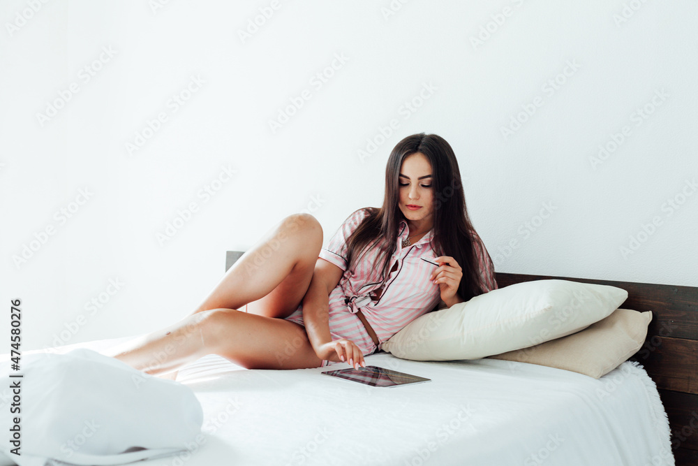 Obraz premium beautiful brunette woman in bed with internet tablet online