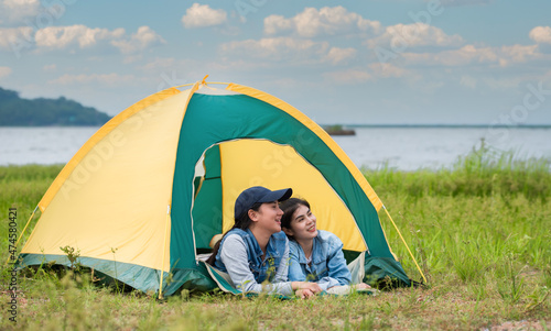 Happy two Asian woman lying down in the tent while camping on meadow near lake in parks and outdoor on vacation.