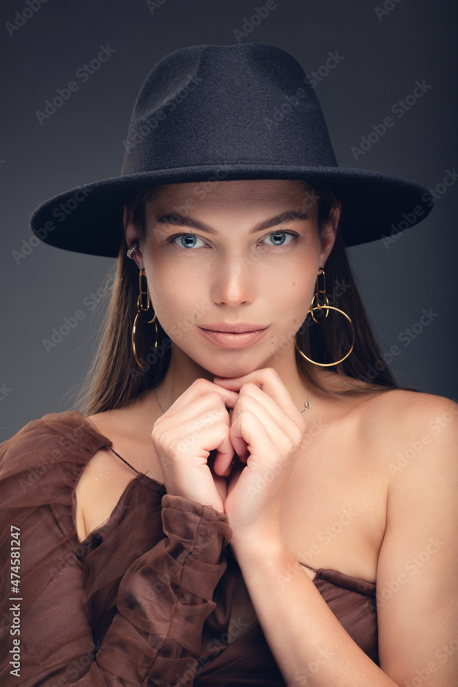 Fashionable studio portrait of a beautiful young girl in black hat on a grey background. Fashionable studio portrait of a beautiful young girl in black hat on a grey background.
