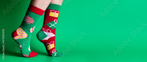 Feet of obscured child in Christmas socks walking on tiptoes against green background