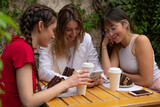 Three friends having a coffee in a restaurant, one of her showing them something on her mobile and laughing.
