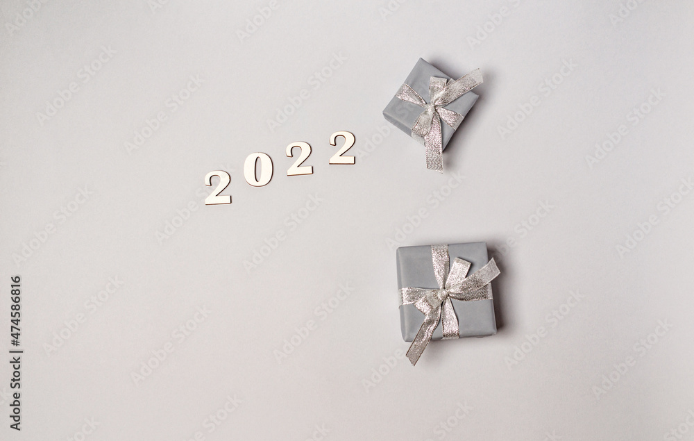 Wooden white numbers 2022 and gift boxes with silver ribbons on a gray background with place for text, copy space.