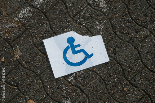 A torn and wet disabled person sign on the ground photo