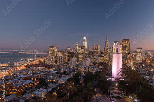 Nighttime aerial view of the San Francisco skyline with Coit Tower prominent in the frame. Bay Bridge in the background. photo