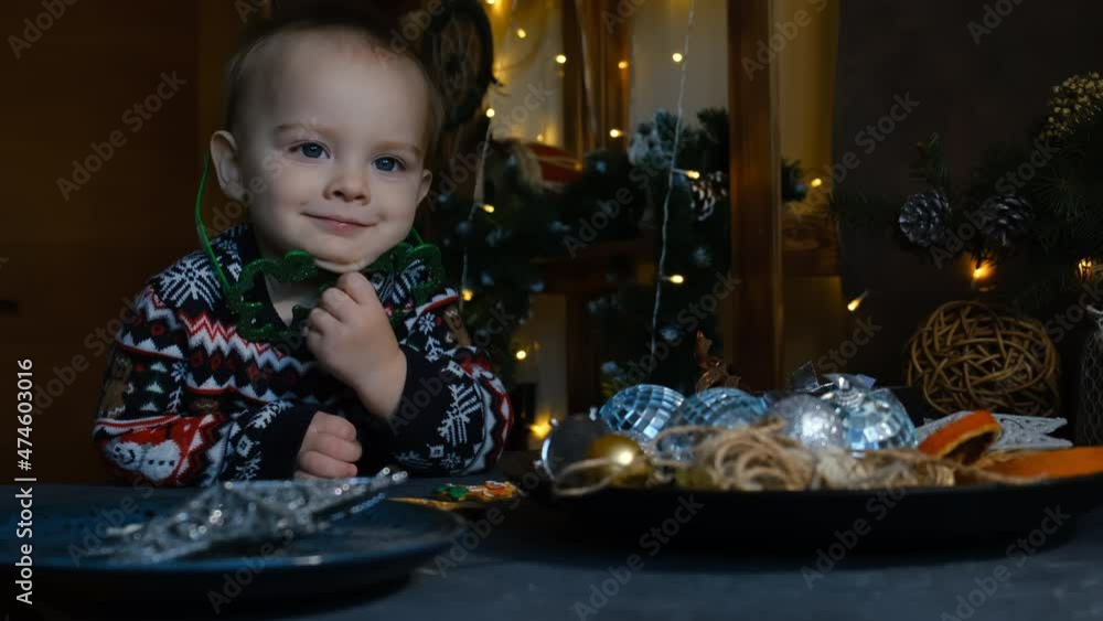 Adorable little boy in Christmas sweater dreamily looks and waits for Christmas time surrounded by Xmas interior and decorations at home. Holiday home decorating, Xmas preparation concept. Adorable little boy in Christmas sweater dreamily looks and waits for Christmas time surrounded by Xmas interior and decorations at home. Holiday home decorating, Xmas preparation concept.