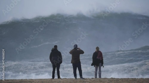 Slow motion of a wave break on the beach in Nazaré, Portugal. Some tourists watching the wave break.