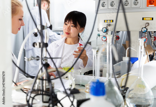 Intelligent yuong Chinese girl working with reagents in test tubes during chemical experiment with female groupmate in student lab