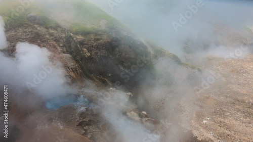 A geyser erupts on the hillside. Blue water in the boiler is visible, splashes and clouds of steam. Valley of Geysers. Kamchatka