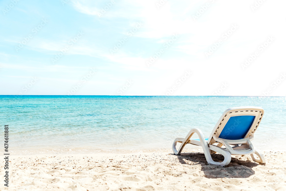 A lone white blue sun lounger stands on the seashore right next to the water. The concept of a beach holiday by the sea or ocean. Private beach of the hotel. Quiet calm sea side. High quality photo A lone white blue sun lounger stands on the seashore right next to the water. The concept of a beach holiday by the sea or ocean. Private beach of the hotel. Quiet calm sea side. High quality photo