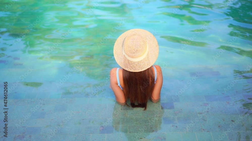 Back to the camera. A woman relaxes on the shallow stop of a resort swimming pool. Title space