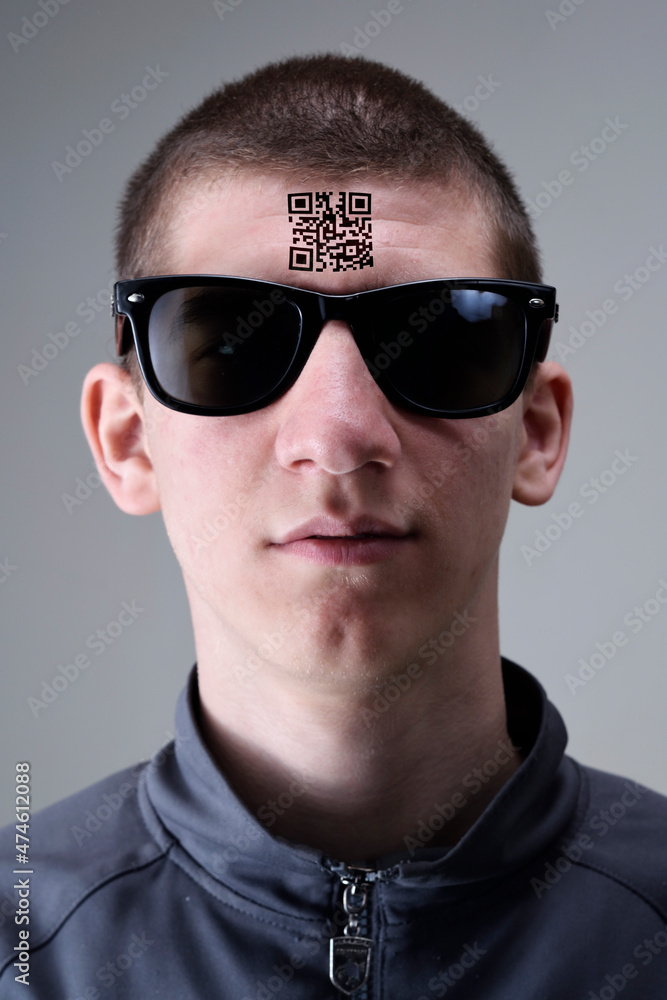 Fototapeta premium Young man with glasses presents a tattoo with a QR code on his forehead.