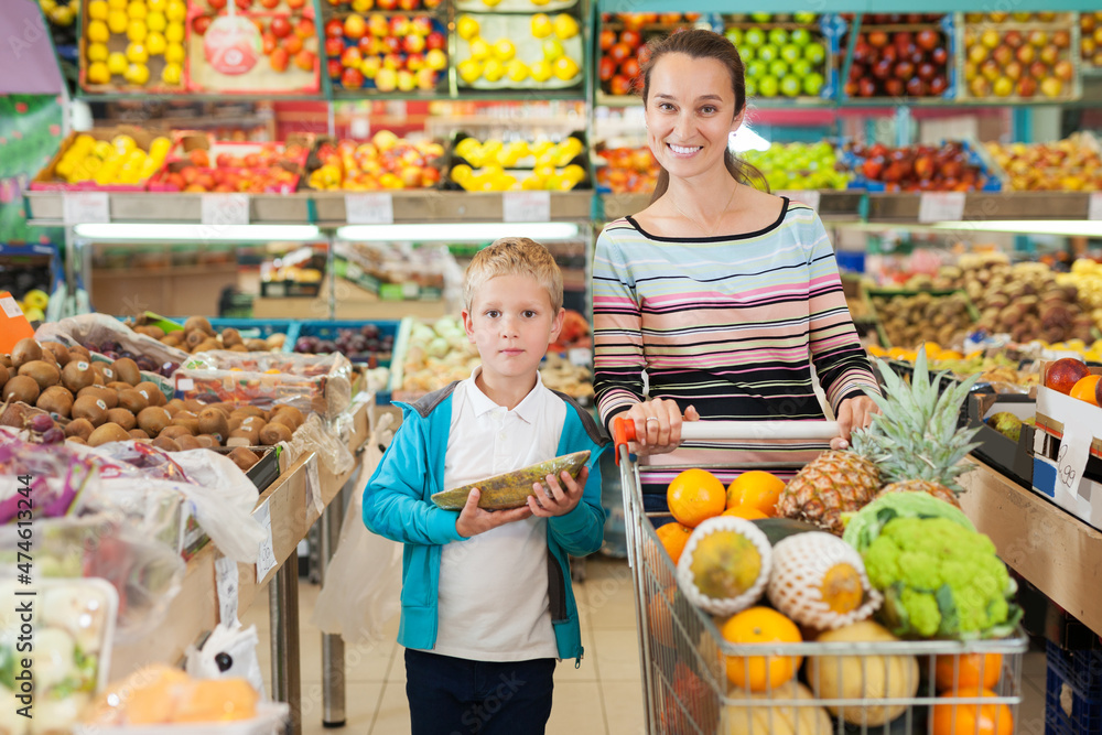 Cheerful positive mother with little boy buying fruits and vegetables at store