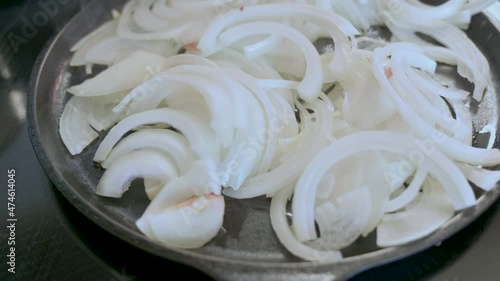 Sliced white onions sauce in oil in cast iron pan on stove, homemade photo