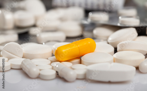 Yellow drug capsule lying among white tablets. Conceptual image of unique treatment