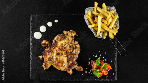 Grilled chicken meal with fries in a basket on a black plate with sauces and fresh veggies