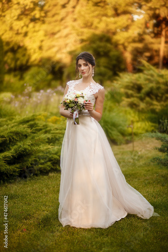 A beautiful bride in a white dress holds a wedding bouquet in her hand. Bride on a walk on a warm autumn day. Portrait of a happy wedding bride on their wedding day.
