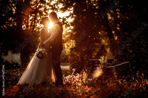 Foto Bride and groom stand in a beautiful green garden on a warm autumn day