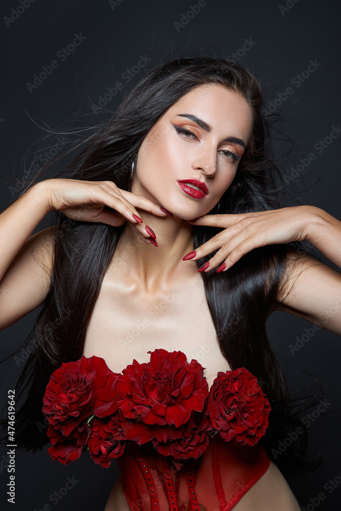 Naklejka premium Beautiful brunette woman with a bouquet of red rose flowers in red corset. Long hair, nude slim body art portrait