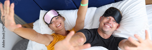 Smiling man and woman in sleep masks lie on bed