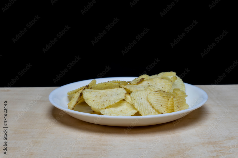 Salted Potato Wafers in White Dish on Wooden Table, Heap of Wafers, Copy Space, Heap of Chips, Side View, Isolated In Black Background Salted Potato Wafers in White Dish on Wooden Table, Heap of Wafers, Copy Space, Heap of Chips, Side View, Isolated In Black Background