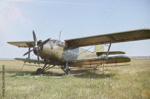 An old Soviet AN 2 aircraft of protective color stands at the airfield in a green field