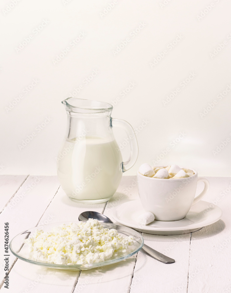 Fresh cow's milk in a jug on a white background with healthy cottage cheese and a cup of coffee with marshmallows Fresh cow's milk in a jug on a white background with healthy cottage cheese and a cup of coffee with marshmallows