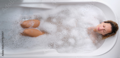 A young woman lies in a soapy foam bath, top view