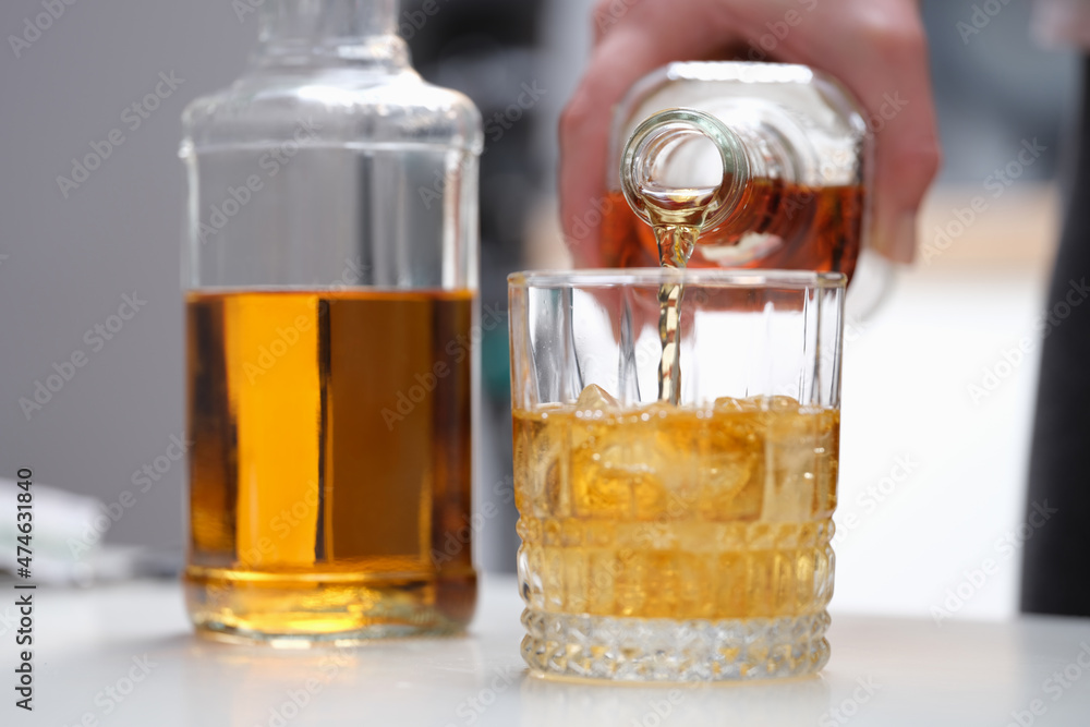 A hand pours a brown alcoholic drink into a glass A hand pours a brown alcoholic drink into a glass