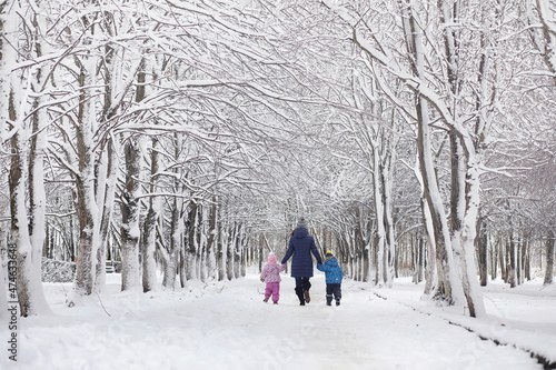 Snow-covered winter park and benches. Park and pier for feeding ducks and pigeons.Family on a walk in the snow covered the park. © alexkich