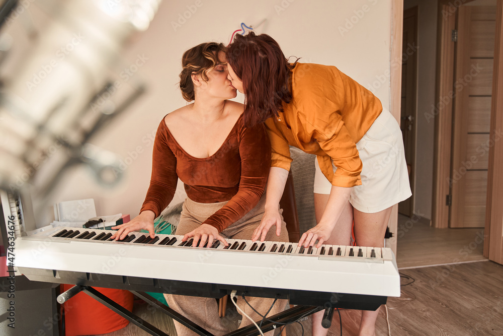 Lesbian girls standing at the piano and kissing each other while spending  time at home Stock Photo | Adobe Stock