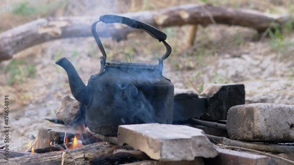 Old Black Smoked Kettle Warms Itself on the Grate of a Blazing, Fading Bonfire. Dirty coffee pot on a campfire. Boiling teapot on an open fire. Concept of adventure, travel, hiking, camping. Close up. Old Black Smoked Kettle Warms Itself on the Grate of a Blazing, Fading Bonfire. Dirty coffee pot on a campfire. Boiling teapot on an open fire. Concept of adventure, travel, hiking, camping. Close up.