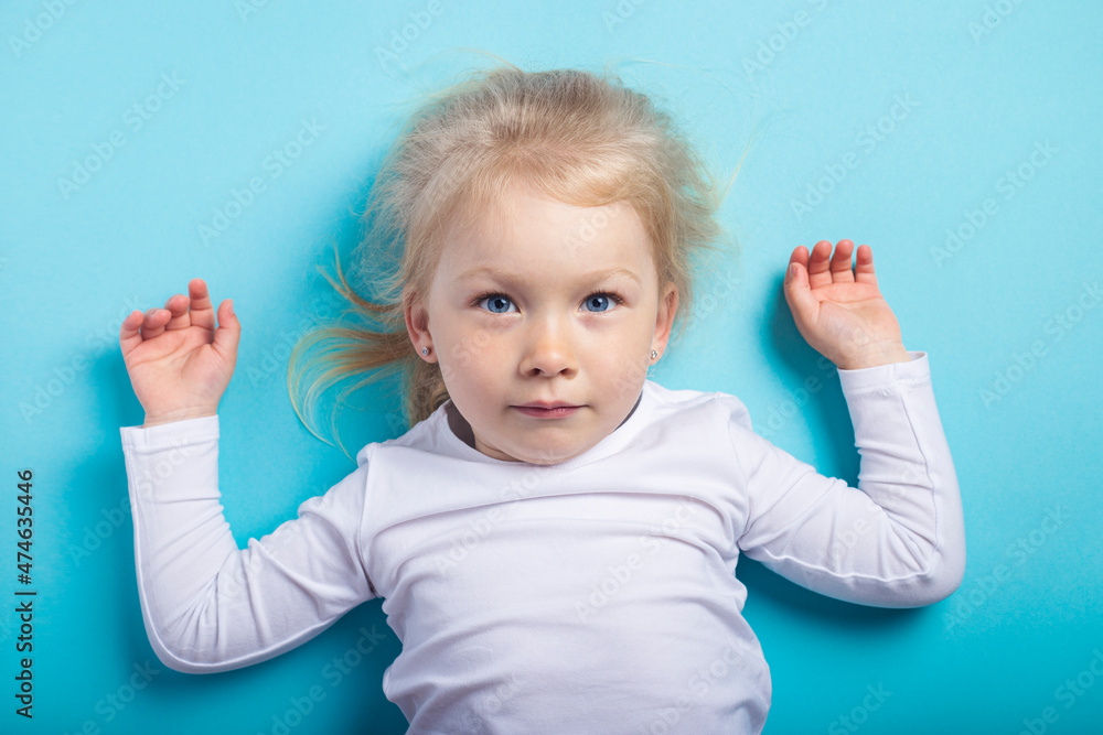 Beautiful blonde girl lying on a blue background. Top view, flat lay Beautiful blonde girl lying on a blue background. Top view, flat lay
