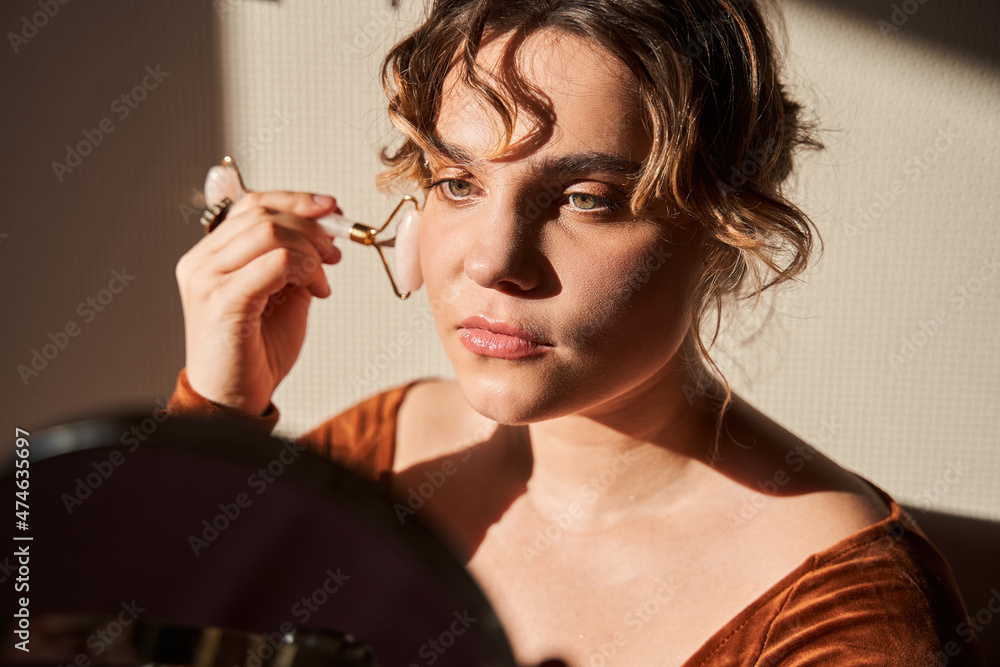 Obraz premium Curly beautiful lady with mirror in hands is starting morning with massaging skin