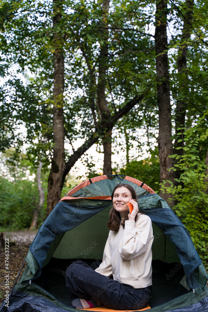 Woman talking on the phone on a hike. Use of mobile communication in a tent in the forest. Call from the office during vacation Woman talking on the phone on a hike. Use of mobile communication in a tent in the forest. Call from the office during vacation