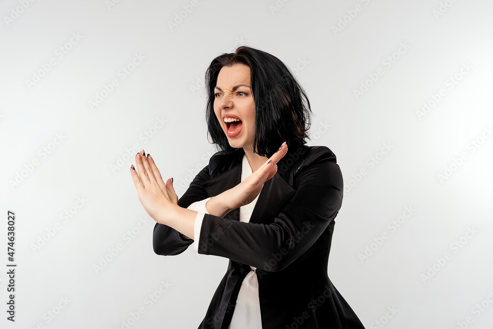 Serious young businesswoman in black formal jacket white shirt shows cross stop gesture with an angry aggressive expression, standing over white background. Business concept Serious young businesswoman in black formal jacket white shirt shows cross stop gesture with an angry aggressive expression, standing over white background. Business concept