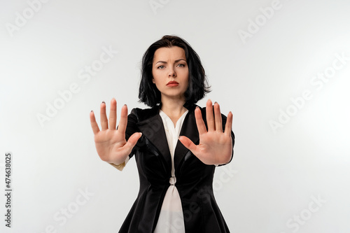 Serious young businesswoman in black formal jacket white shirt showing stop gesture with palms isolated on white background. Social distancing. New normal behavior. Business concept