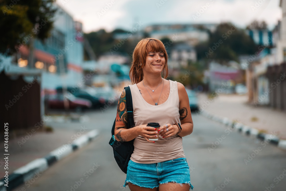 Portrait of happy young woman with tattoo walking with a cup of coffee in her hands. Evening stroll and vacation
