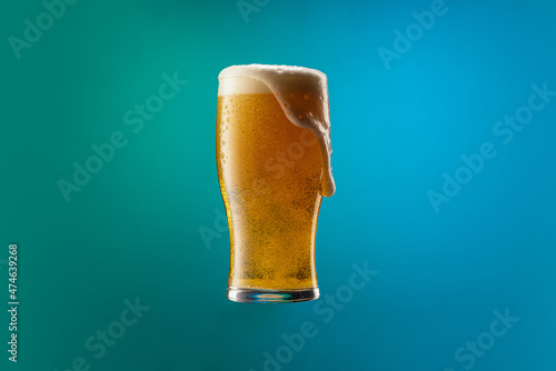 Tablou canvas Full glass of frothy light lager beer isolated over gradient blue and green color background in neon