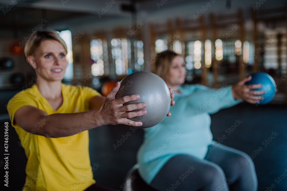 Personal trainer training overweight woman, sitting on fintess bal and  exercising in gym. Stock Photo | Adobe Stock