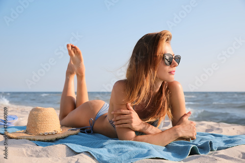 Attractive woman with sunglasses sunbathing on beach towel near sea