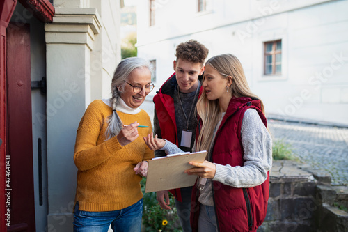 Young door to door volunteers talking to senior woman and taking survey at her front door.