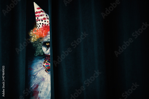 Obraz na plátně Terrifying clown hiding behind black curtains, space for text
