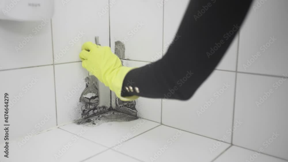 A woman's hand in a yellow rubber glove cleans dirt with a sponge on a white tile A woman's hand in a yellow rubber glove cleans dirt with a sponge on a white tile
