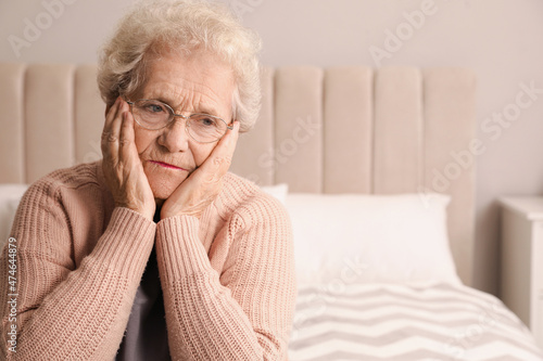 Senior woman with headache in bedroom at home. Space for text